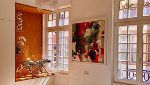 Une chambre à coucher avec un lit, un lustre, une fenêtre donnant sur un beau paysage et un tableau accroché au mur.
