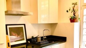 Une cuisine compacte avec des meubles blancs, une hotte en acier inoxydable, un four encastré et un plan de travail noir.