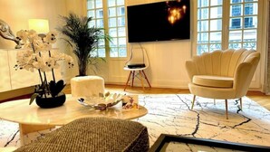 Un salon moderne doté d’un grand téléviseur, d’un canapé, d’une table basse agrémentée d’objets décoratifs et d’une grande fenêtre offrant une vue sur les bâtiments.