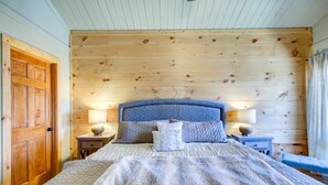 A bedroom with a wooden headboard, a large bed with a patterned blanket, two bedside tables with lamps, and a wooden door. - Beech Mtn: Walk to Slopes, Sleeps 9, Pet Friendly, Mountain Views, Cozy Retreat (Beech Mountain)