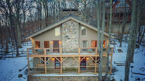 A two-story cabin with a stone facade, wooden balconies, and a snow-covered ground. - Beech Mtn: Walk to Slopes, Sleeps 9, Pet Friendly, Mountain Views, Cozy Retreat (Beech Mountain)