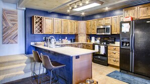 A modern kitchen with wooden cabinets, a central island with bar stools, a stainless steel refrigerator, and a microwave. - Beech Mtn: Walk to Slopes, Sleeps 9, Pet Friendly, Mountain Views, Cozy Retreat (Beech Mountain)