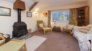 A cozy living room with a fireplace, two armchairs, a sofa, and a window with curtains.