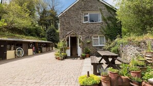 A stone building with a wooden door and windows, surrounded by potted plants and a picnic table.