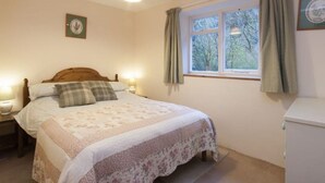 A bedroom with a bed, two bedside tables, a window with curtains, and a wall-mounted light fixture.