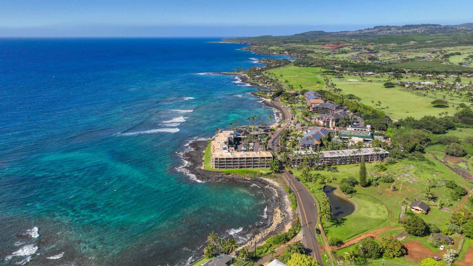 An aerial view of a coastal property with a large building, a golf course, and clear blue waters.