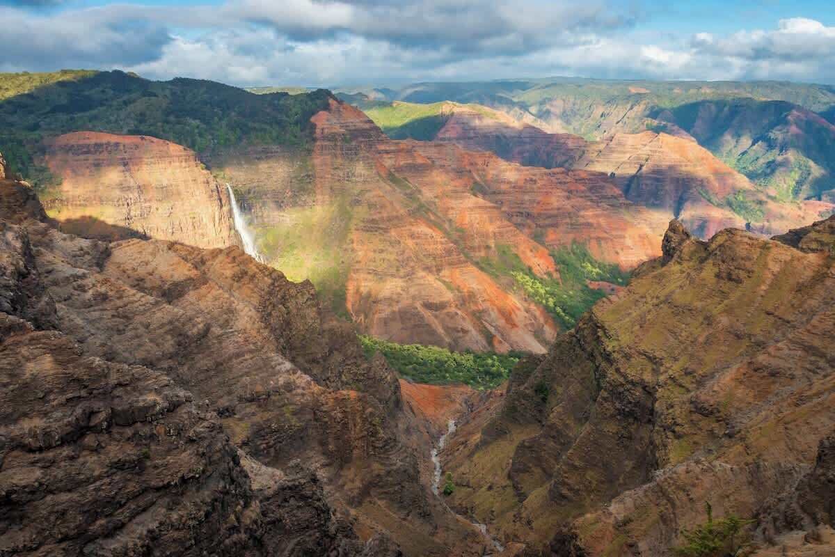 Paisagem de cânion com formações rochosas estratificadas e uma cascata.