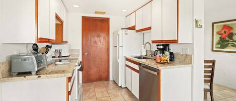 A compact kitchen with white cabinets, a wooden door, a refrigerator, a sink, and a countertop with various items.