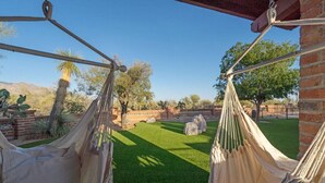 A hammock set up on a patio with a view of a well-maintained lawn and a brick wall. - Spacious casita with desert & mountain views ⛰ (Tucson)