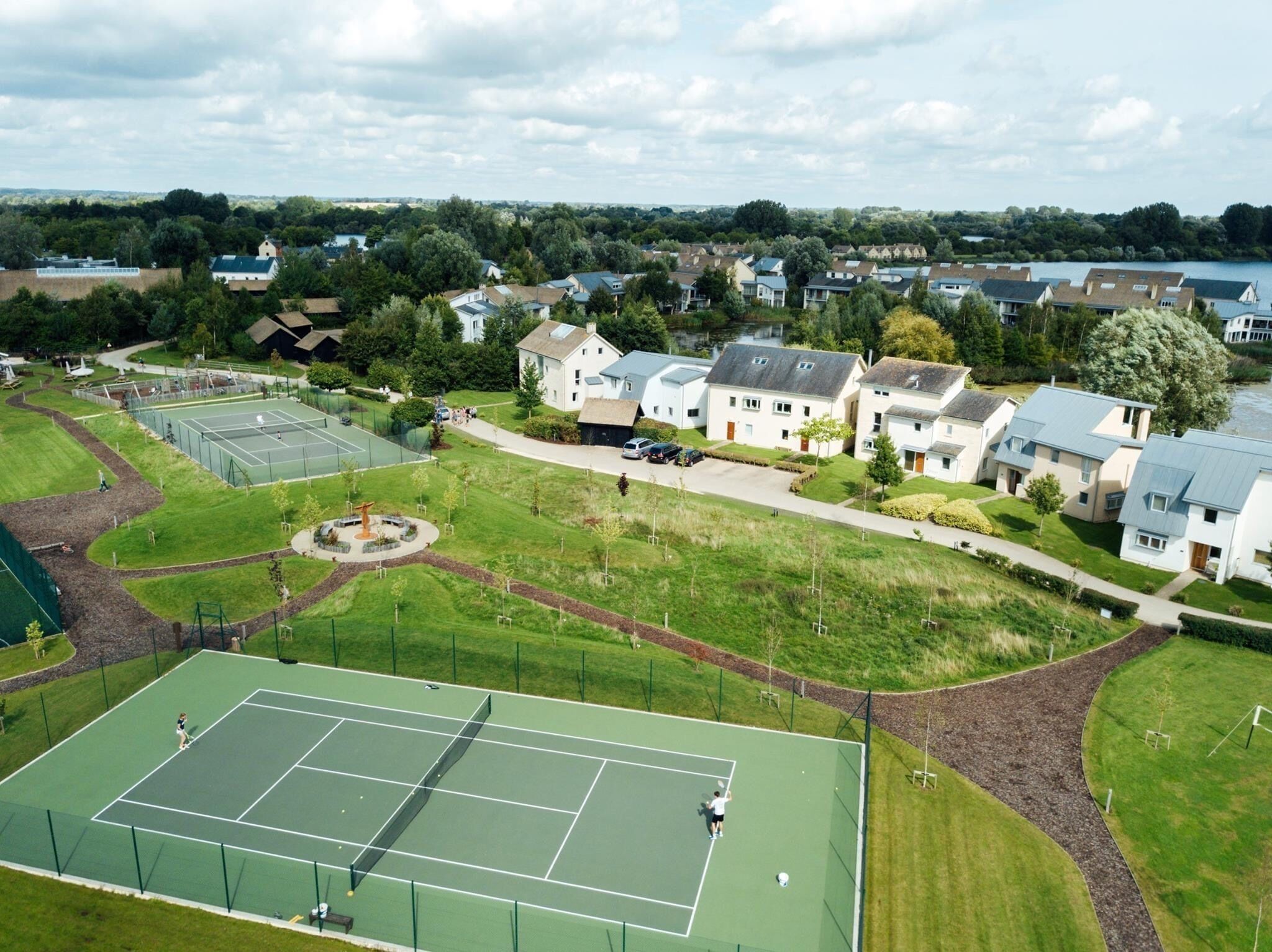 An aerial view of a residential area with houses, a tennis court, and a park.