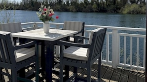 A deck with a table and chairs overlooking a body of water, surrounded by trees. - Peaceful Lakefront Escape w/ Deck & Views (South Cerney)