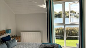 Un dormitorio con una cama grande, una mesita de noche y vistas a un lago a través de una ventana.