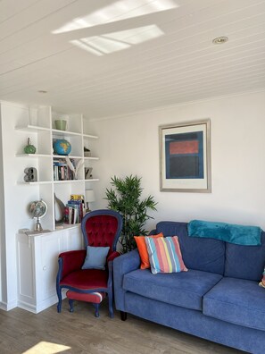 Een woonkamer met een blauwe bank, een rode fauteuil, een boekenkast en een lijst met een afbeelding aan de muur.