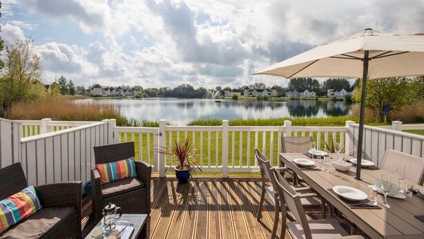 Una terraza con mobiliario exterior, una mesa de comedor para dos personas y vistas a un lago.
