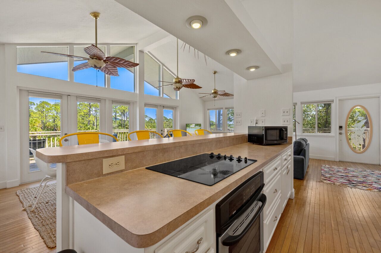 A modern kitchen with a central island, overhead fans, and large windows.