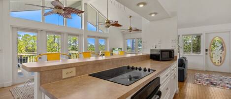 A modern kitchen with a central island, overhead fans, and large windows.