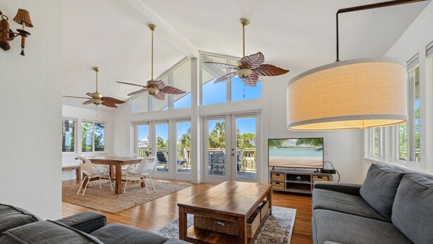 A spacious living area with a large window, ceiling fans, a dining table, and a sofa. - Kayak Cove: Bayfront with dock - A paddle in / paddle out resort (Cedar Key)