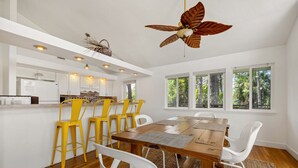 A modern kitchen with white cabinets, a wooden dining table, and yellow chairs. - Kayak Cove: Bayfront with dock - A paddle in / paddle out resort (Cedar Key)