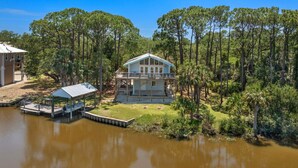 A house with a dock, surrounded by a forest and a body of water. - Kayak Cove: Bayfront with dock - A paddle in / paddle out resort (Cedar Key)