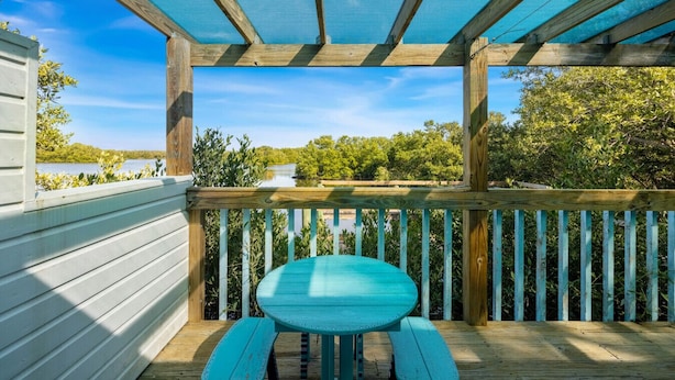 A wooden deck with a table and benches, overlooking a body of water and greenery.