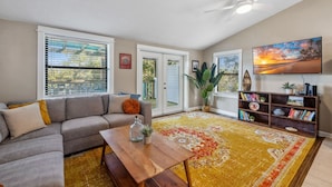 A living room with a sofa, coffee table, bookshelf, and a large window with blinds.