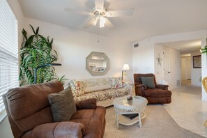 A living room with a ceiling fan, a sofa, a chair, a coffee table, and a large plant.