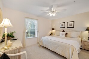 Une chambre à coucher comprenant un lit, des tables de chevet, un bureau, un ventilateur de plafond et une fenêtre avec des rideaux.