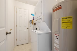 Une buanderie avec un lave-linge et un sèche-linge blancs, une porte et une étiquette « GUIDE ÉNERGÉTIQUE » apposée sur le sèche-linge.