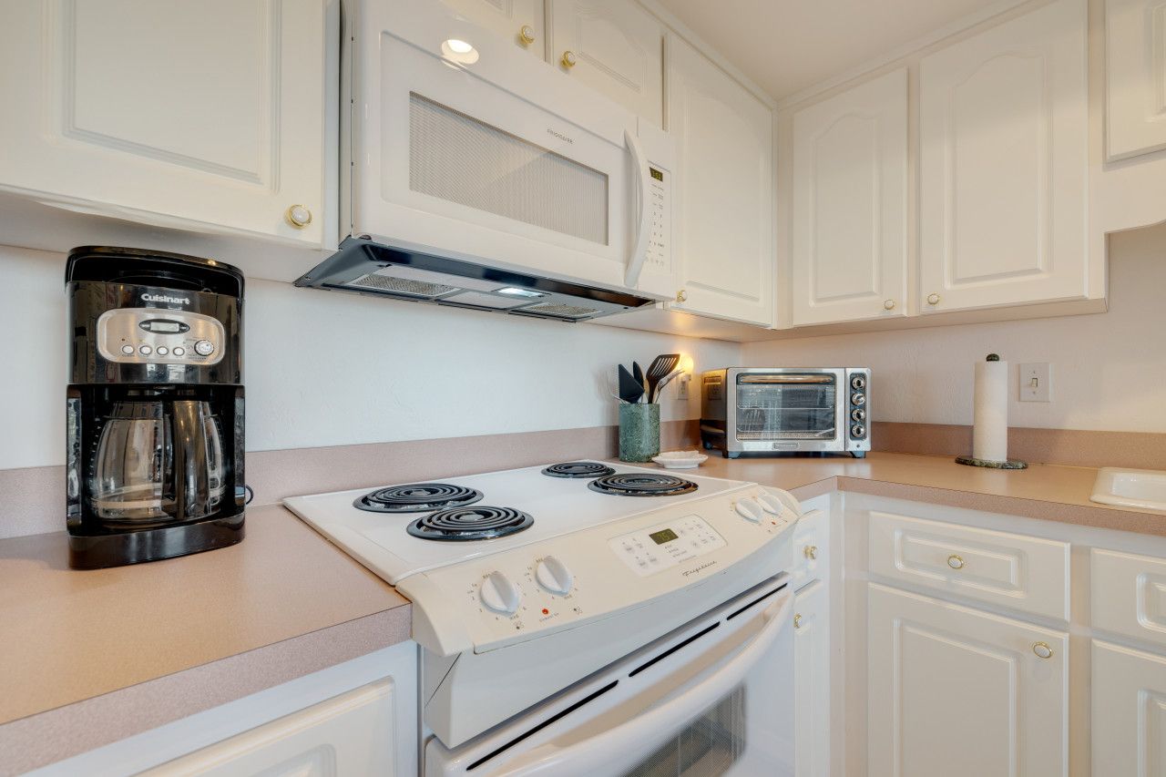 A modern kitchen with white cabinets, a built-in microwave, a coffee maker, a toaster, and a stove.