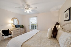 A bedroom with a bed, a chair, a dresser, a ceiling fan, and a window.