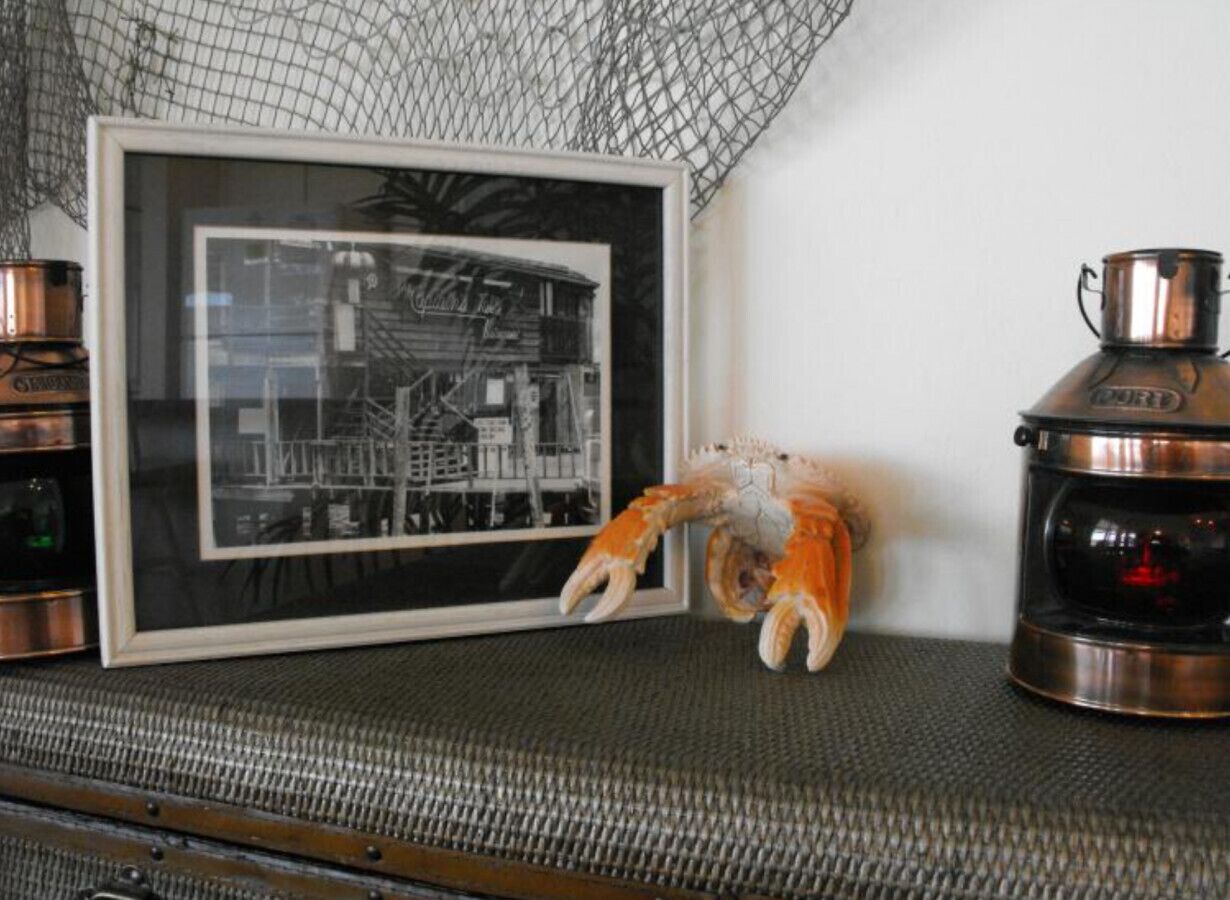 Une photographie en noir et blanc encadrée représentant un bâtiment, une décoration en forme de crabe en céramique et un récipient en acier inoxydable.