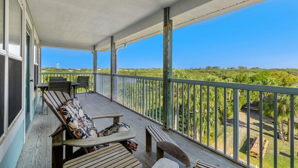 A covered outdoor deck with wooden furniture and a view of a lush landscape. - Above the Rest B301:  A spacious penthouse with water views (Cedar Key)