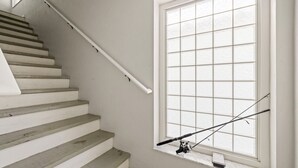 A staircase with a white railing and a window with a fishing rod hanging on the sill.
