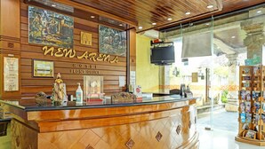 A reception desk with a wooden finish, a mounted television, and a glass door leading outside. - Collection O 91081 New Arena Hotel (Kuta)