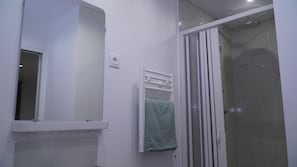 A bathroom with a mirror, a towel rack with a green towel, and a shower area with a glass door.