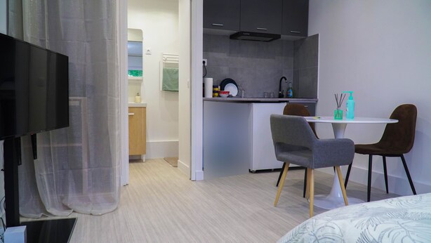 Ein modernes Hotelzimmer mit einem Flachbildfernseher, einem Essbereich mit Tisch und Stühlen sowie einer Küchenzeile mit Spüle und Schränken.