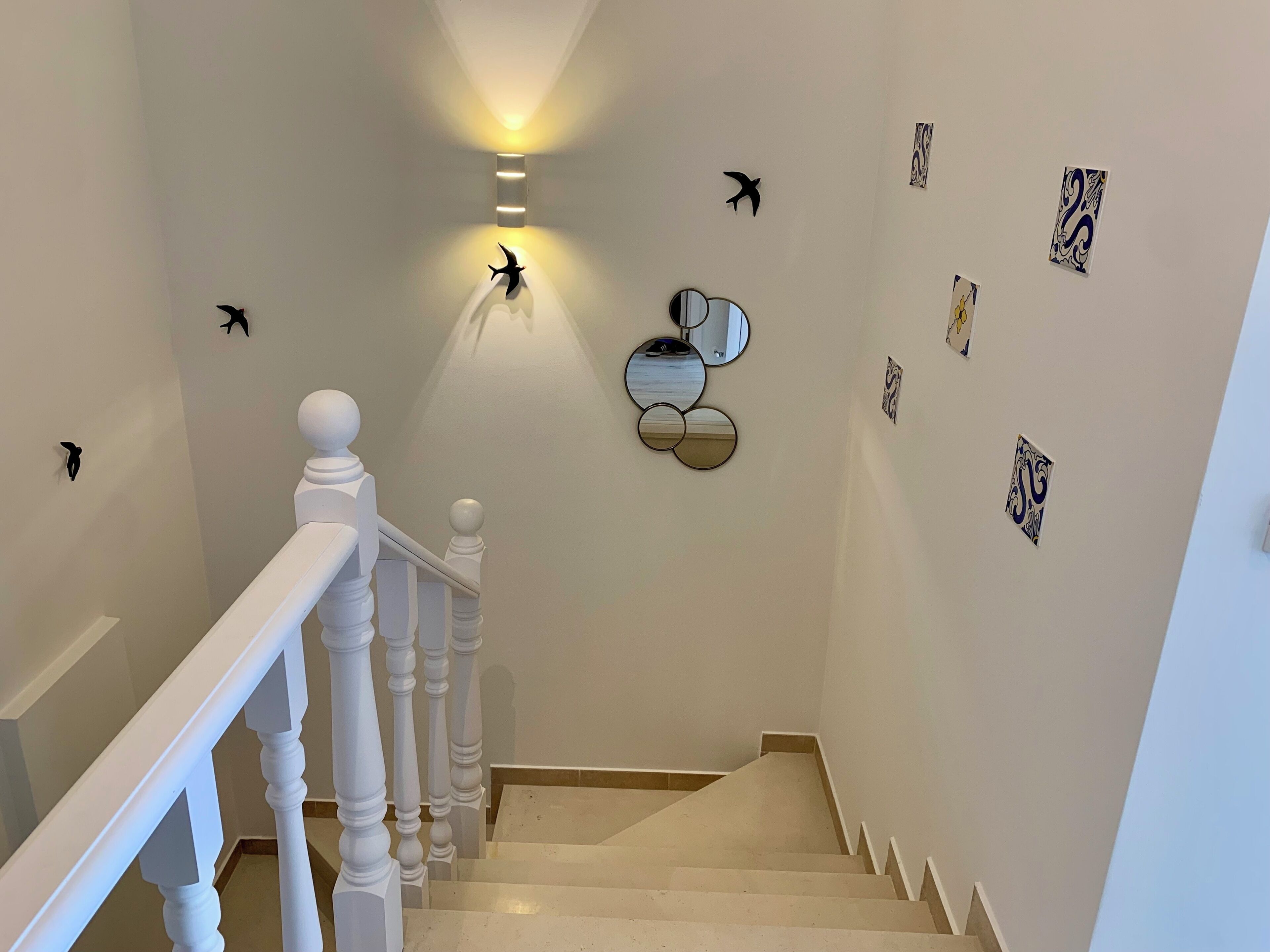 A staircase with a white railing, a wall-mounted light fixture, and decorative wall art including bird silhouettes and abstract designs.