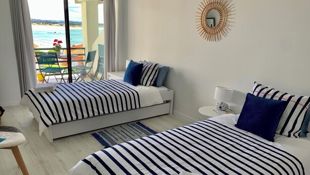 Une chambre d’hôtel avec deux lits, une vue sur la plage, une décoration murale en forme de soleil et une petite table ronde avec une lampe.