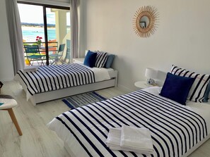 A hotel room with two beds, a view of the beach, a sunburst wall decoration, and a small round table with a lamp.