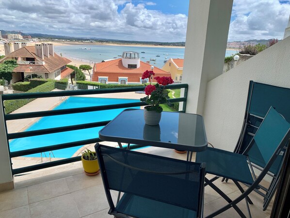 A balcony with a pool, a table with a potted plant, and chairs.