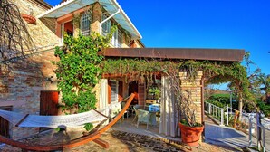 Ein traditionelles Steinhaus mit Anbauten aus Glas, einer Hängematte und einer Terrasse mit Gartenmöbeln.