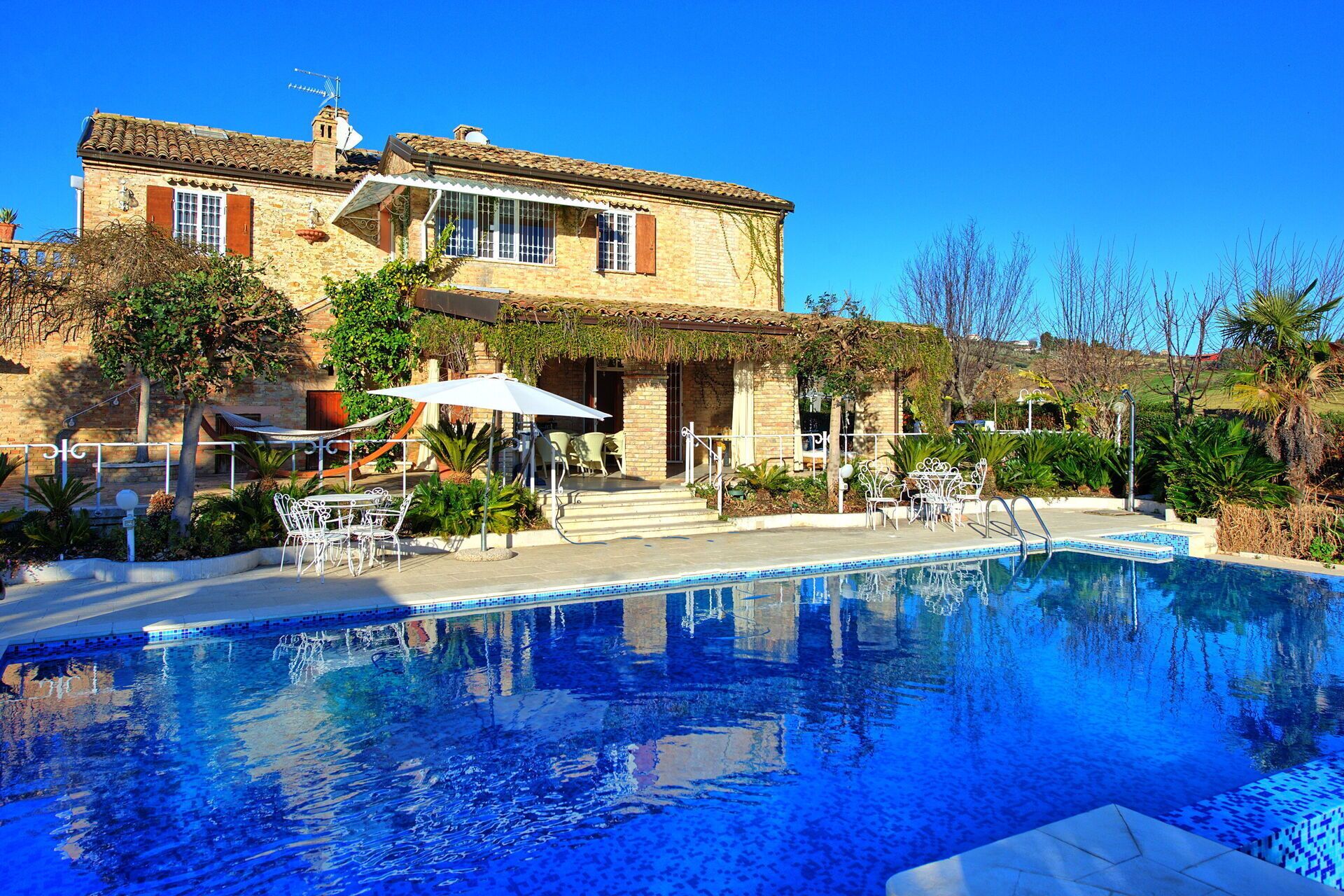 Un área de piscina con un edificio de piedra, asientos al aire libre y una piscina azul cristalina.