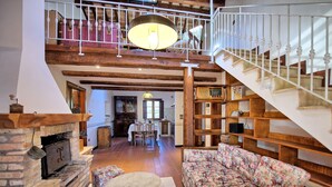 Ein geräumiger Wohnbereich mit Kamin, einem blumigen Sofa und einer Treppe, die in ein Obergeschoss führt.