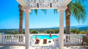 Ein Poolbereich mit Pergola, Palmen und Blick auf die Landschaft.