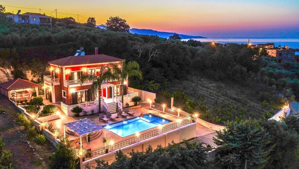 Ein zweistöckiges Haus mit Swimmingpool, umgeben von Grün und mit Blick auf ein Gewässer.
