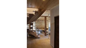 Een modern interieur met een houten trap die leidt naar een vide, een stenen muur en een gezellige zithoek met een flatscreen televisie.