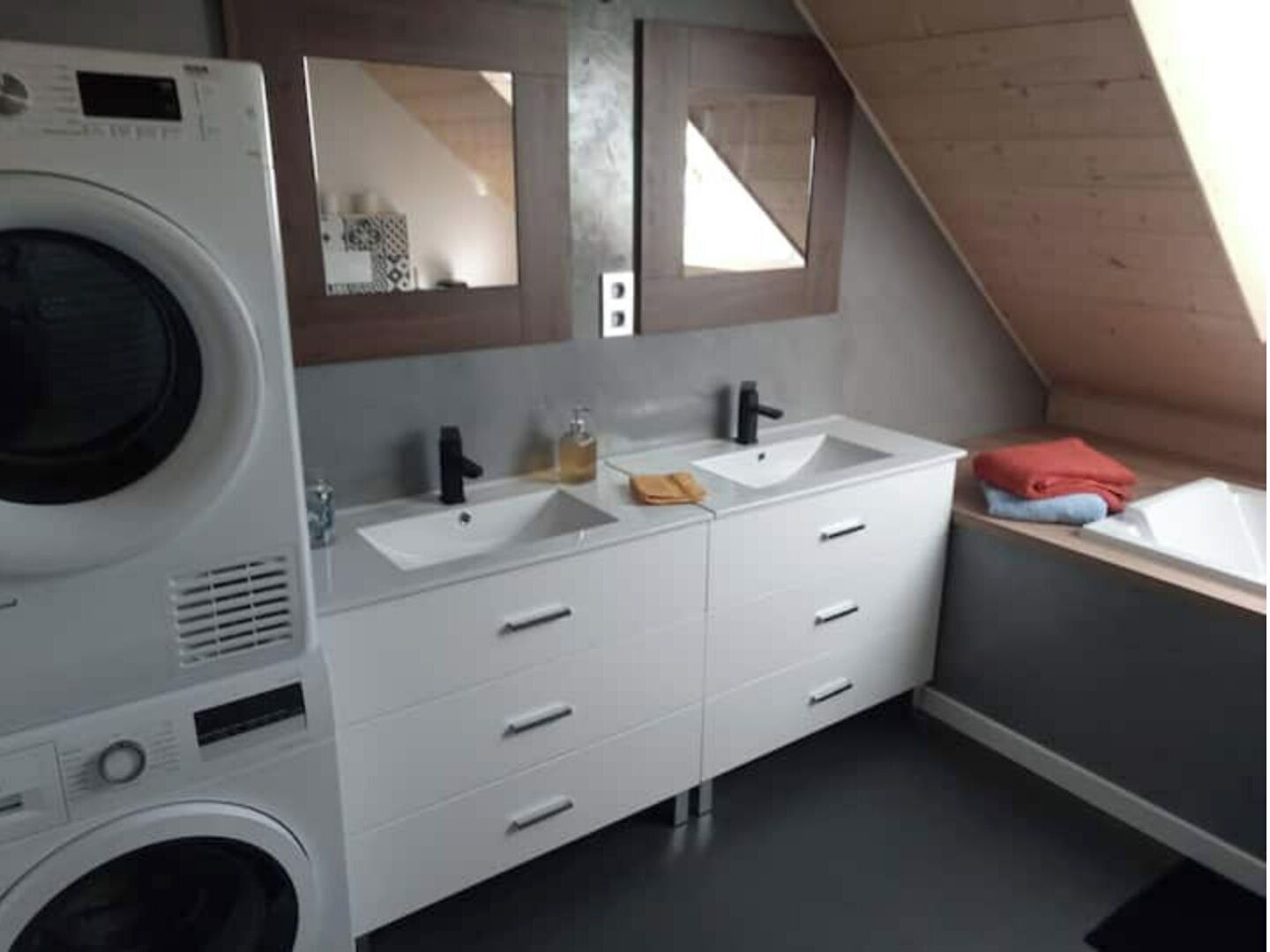 A compact, modern bathroom with a built-in washing machine, two sinks, and a large mirror.