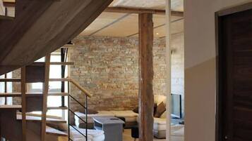 Ein modernes Interieur mit einer Holztreppe, die zu einem Erkerbereich führt, einer Steinwand und einer gemütlichen Sitzecke mit einem Flachbildfernseher.