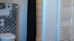 A bathroom with a toilet, a shower curtain, a towel rack, and patterned tiles on the wall. - Grand Appartement Avec Loggia (Orchamps-Vennes)