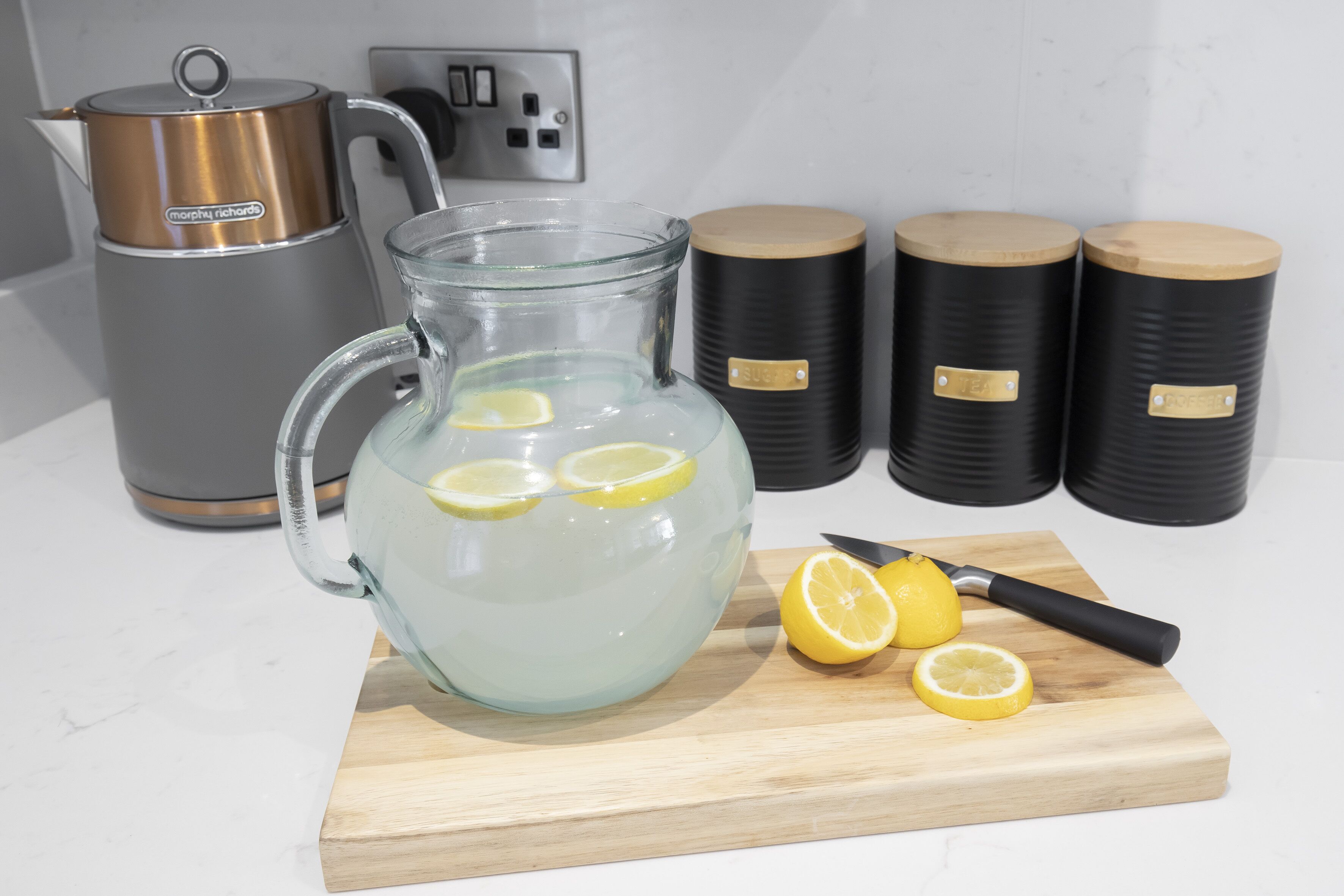 A kitchen with a glass pitcher filled with water and lemon slices, a knife, and a Morphy Richard kettle.